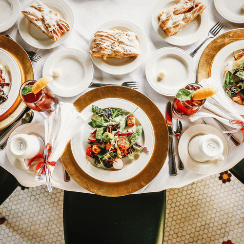 Brunch setup with salads, pastries and iced drinks on white tablecloths and gold-rimmed plates