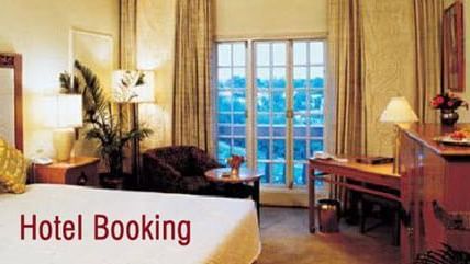 A hotel room interior with a large bed, sofa chair, a table, a cabinet and a table with the text 'Hotel Booking' on the image.