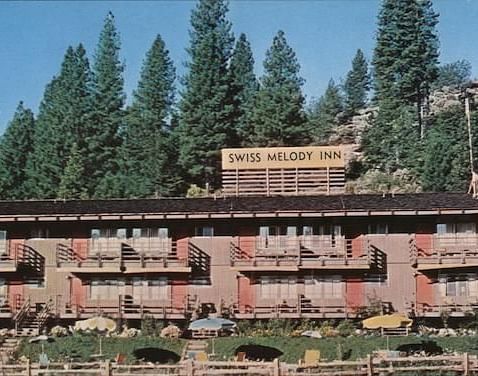 A view of the facade of Narrow Gauge Inn with a backdrop of the forest against blue skies.