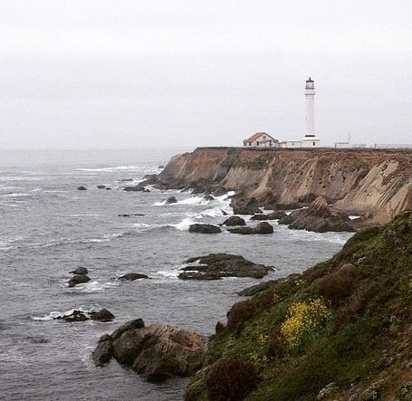 A lighthouse perched on a cliff overlooking the ocean, with waves crashing against the rocky shoreline.