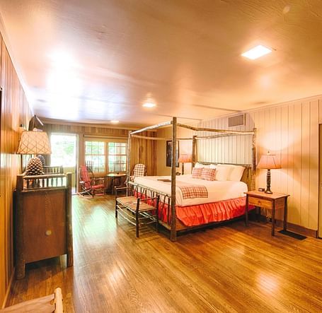 corner view image of a bedroom with a wall mounted picture along with a double bed and a door allowing bright natural light into the room - Historic Tapoco Lodge