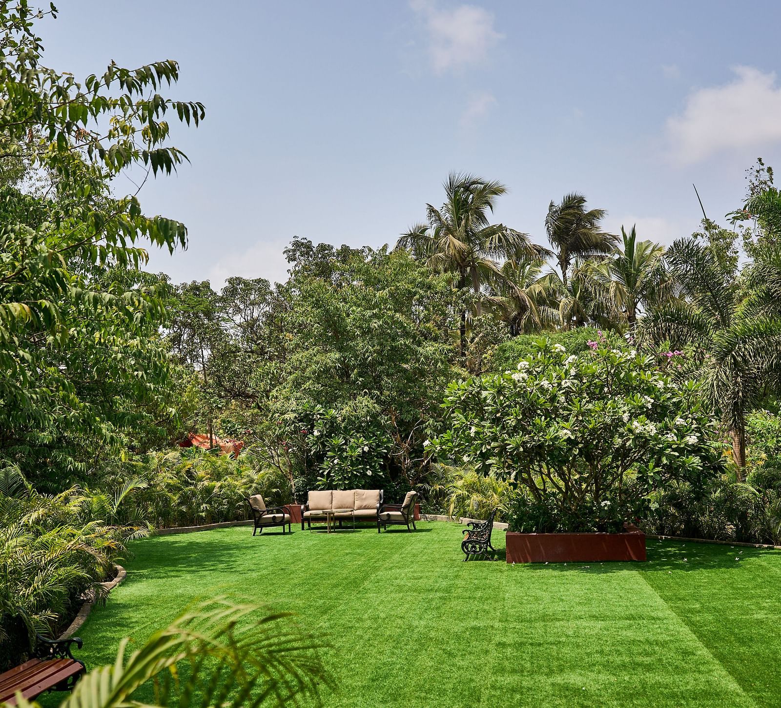 Lawn area encircled by trees and plants, with seating arranged for relaxation at Mayfair Manor, Alibag