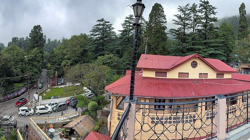 Panoramic view of The Pavilion, Nainital showing terraced gardens with manicured lawns, stone pathways, and traditional architecture against misty hills.