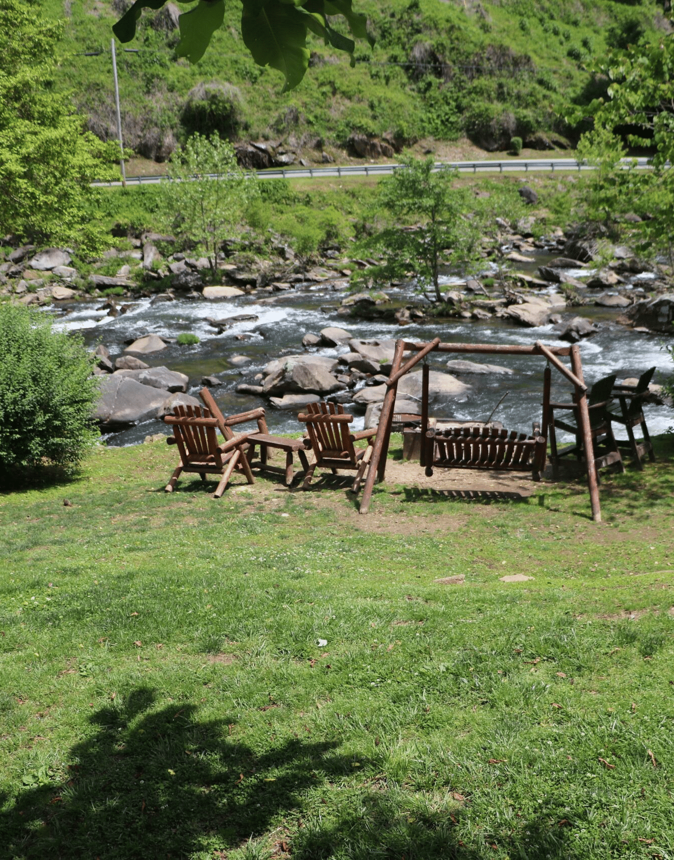 a wooden swing and two wooden arm chairs kept on the bank of a river stream - Historic Tapoco Lodge