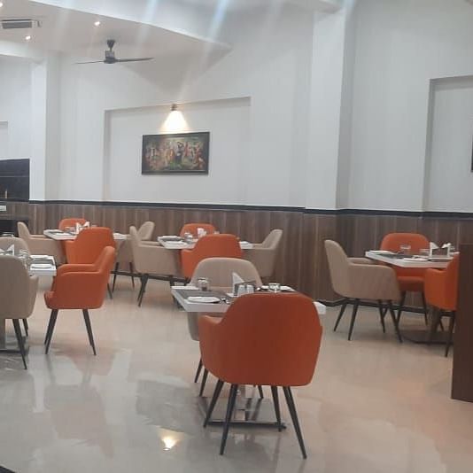 A brightly lit dining area features numerous tables with orange chairs - Kankidham Lords Inn