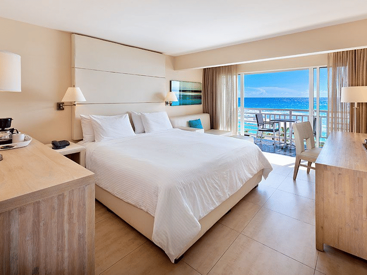 Elegant bedroom with a king size bed, wooden furniture, a balcony and a view of the sea at The Soco Hotel, Barbados.