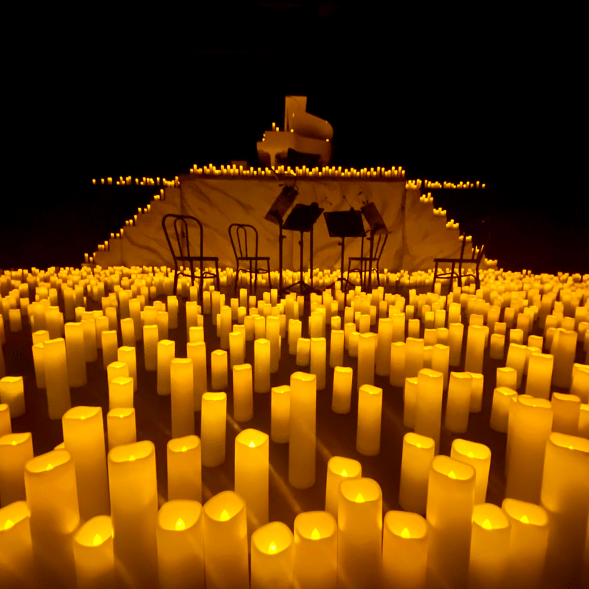 A view of the stage with candlelights all around the stage, chairs in the centre, and a piano on an elevated stage.