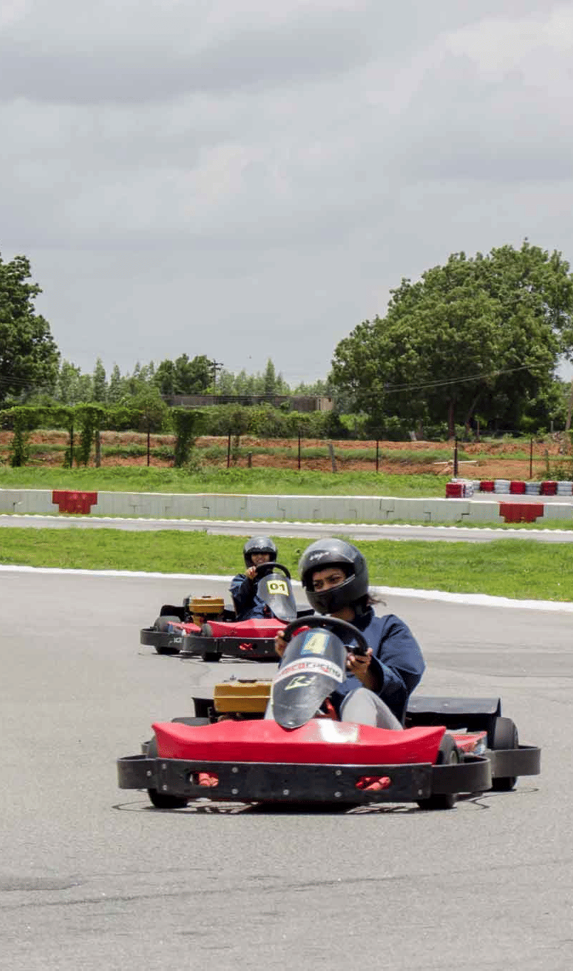 3 people enjoy racing go-karts around a curved outdoor track - District Gravity Adventure Park, Hyderabad