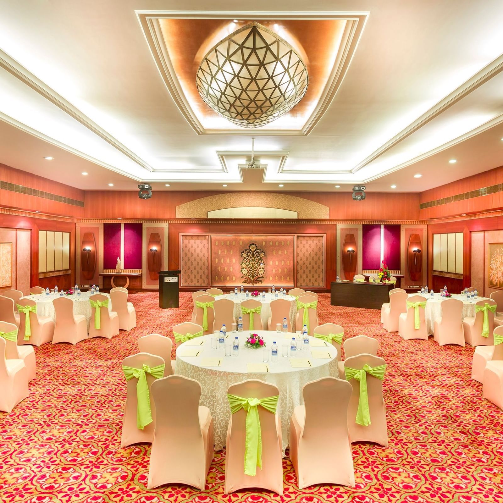 A wedding hall with white chairs tied with yellow ribbons pointing towards the stage at Grand Chennai By GRT Hotels.