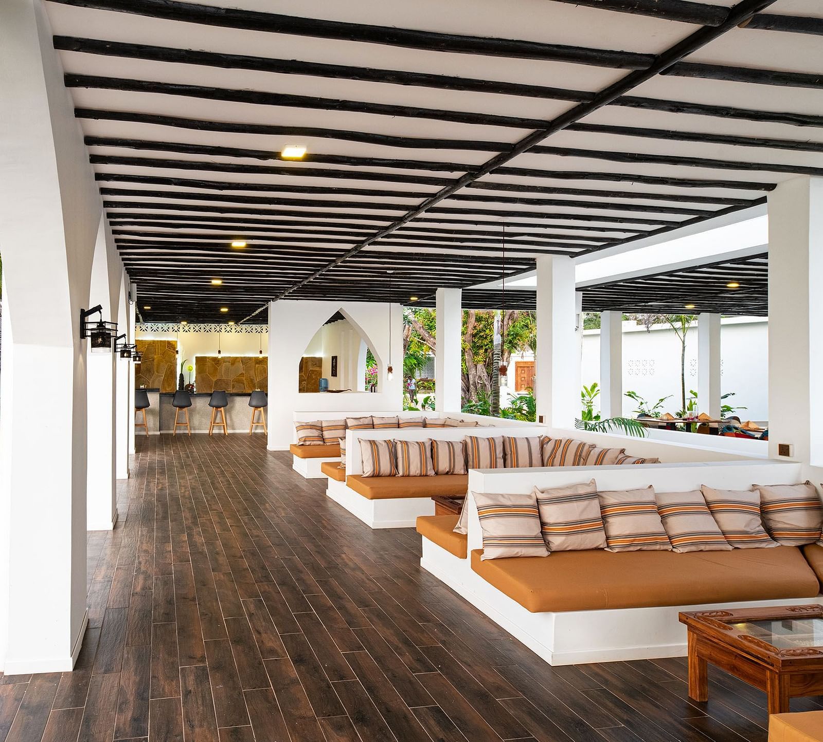 Open-air lounge with long cushioned benches, wooden floors, and garden views through arched openings - Shooting Star Boutique Hotel.