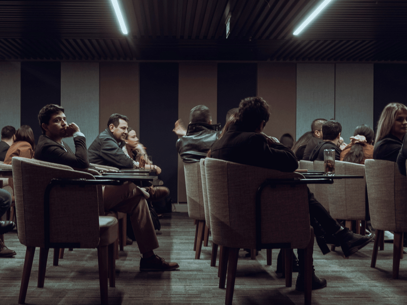 A group of people seated in a conference room, attending a seminar or business discussion, with some attendees engaged and others listening attentively.