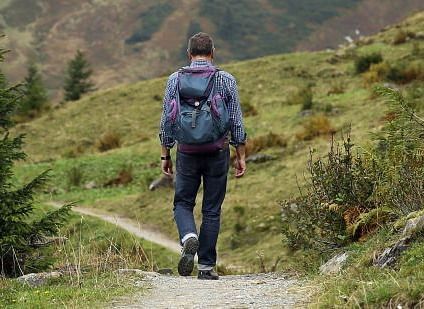 Person with a rucksack walking on a path through a green, hilly landscape.