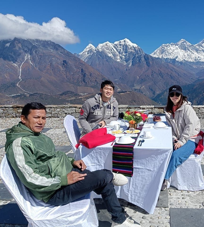 Three people dining outdoors with a stunning mountain range in the background.