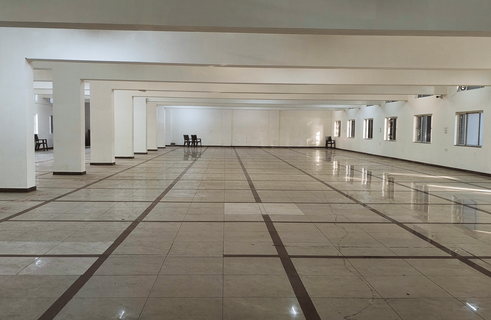 A wide shot of a large, empty banquet hall in BNGV Grandeur Hotel and Banquets, emphasising the hall's length and polished surfaces.