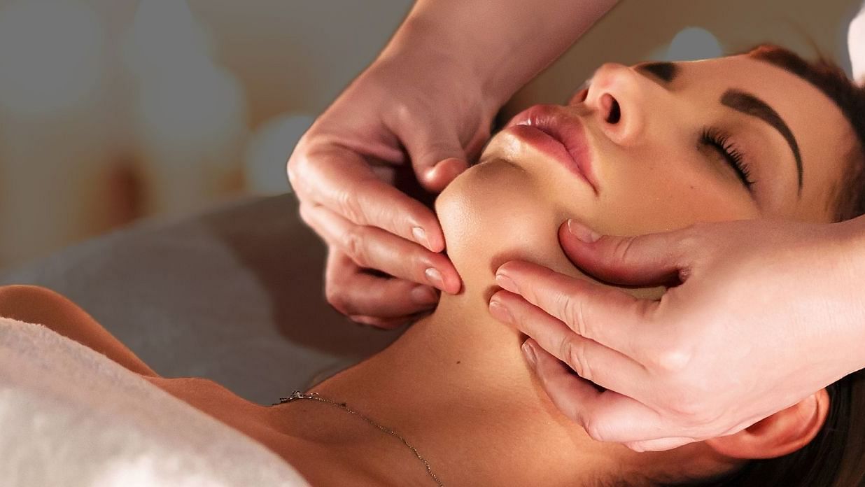 A woman receiving a relaxing facial massage at a luxury spa, with the text Indulgence Begins Here in the background.