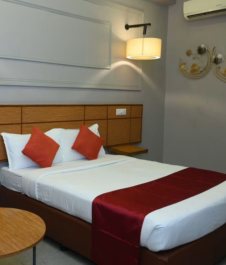 A well-made bed with white linens, red accent pillows and a red runner, in a room at the Max Hotel Prayagraj.