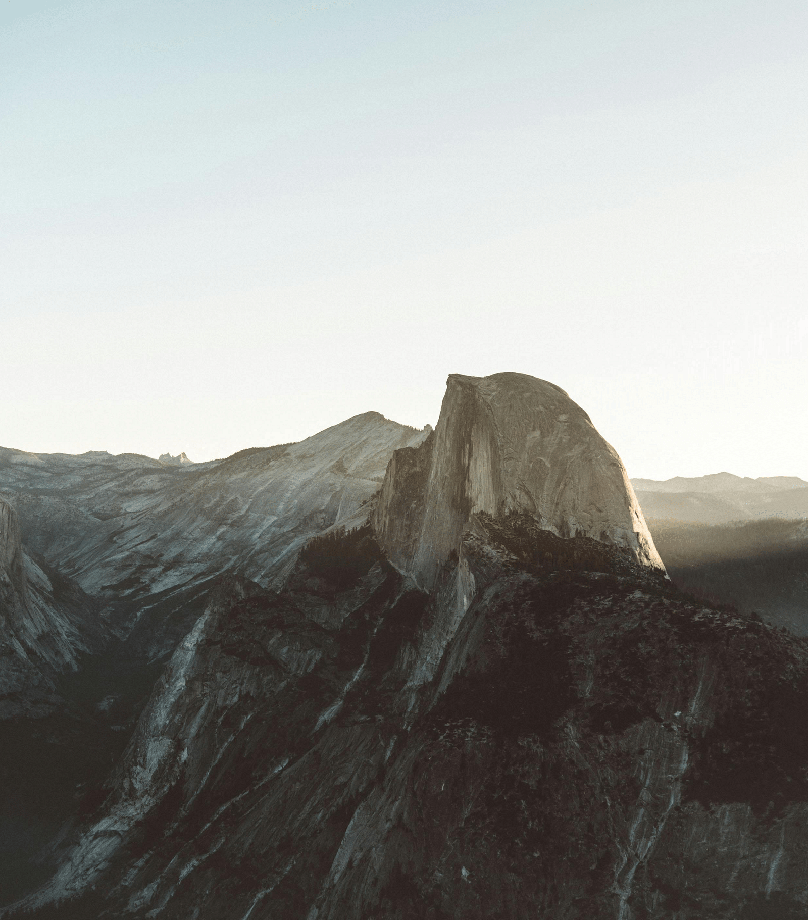 A breathtaking view of a towering peak bathed in soft, golden sunlight, surrounded by rugged mountain ranges.