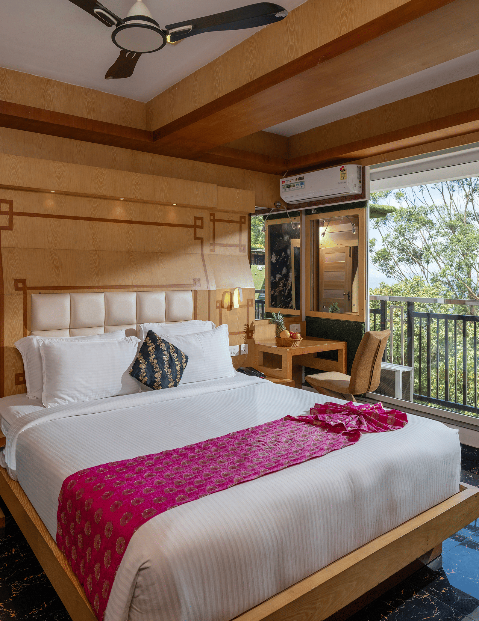 The interior of Superior Room at Parakkat Nature Hotel and Resorts, Munnar featuring a large bed, wooden panelling on the walls and ceiling, a ceiling fan, and a large window overlooking greenery.