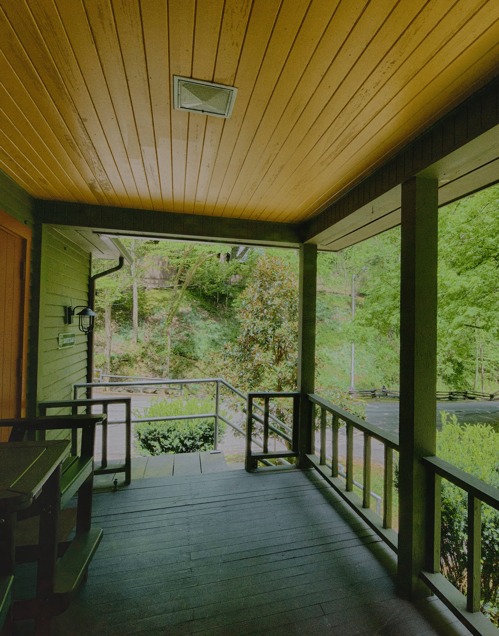 a beautiful wooden porch with hand railings featuring wooden chairs overlooking the serene lush green views of the forest and the trees - Historic Tapoco Lodge