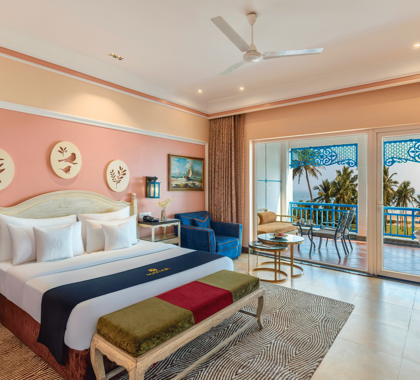 Deluxe room with a king bed, a bench, an armchair and a balcony overlooking the sea and palm trees at MAYFAIR Palm Beach Resort, Gopalpur-on-Sea.