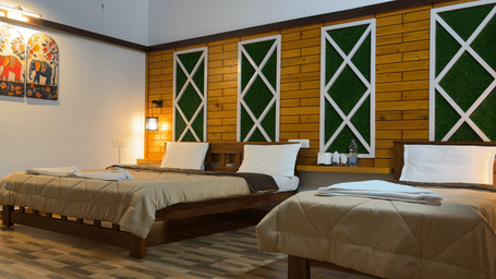 A Family Room With Garden View 2, of Hatti Eden Coorg aturing a large bed with neutral-toned linens and multiple white pillows. The headboard wall is a focal point, decorated with three vertical, rectangular panels of dark textured material accented by lig