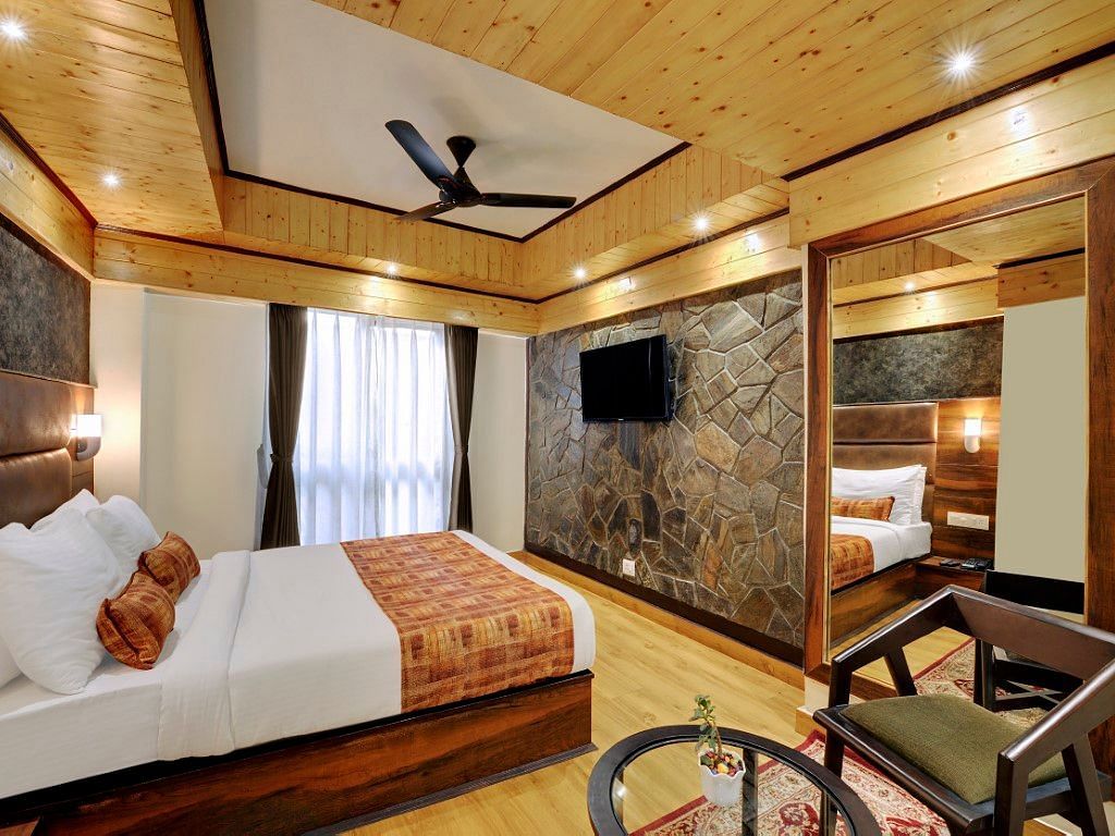 An image of Sumitel Queensyard premium room with king size bed, tv, ceiling fan, and a chair and a table