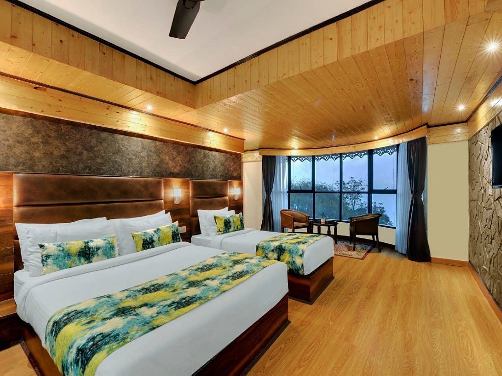 An image of Sumitel Queensyard premium room with king size bed and a single bed, tv, ceiling fan, and a chair and a table