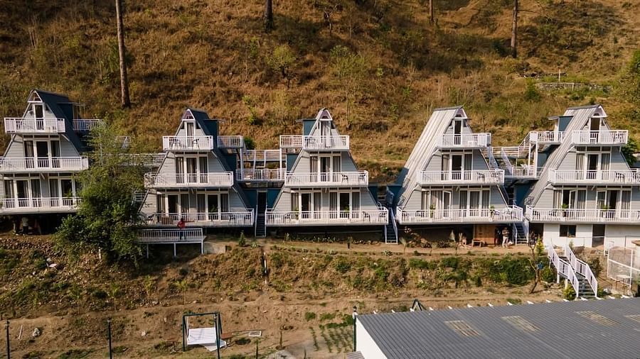 A daytime view of a cluster of white, modern A-frame or pyramid-shaped buildings built on a verdant hillside.