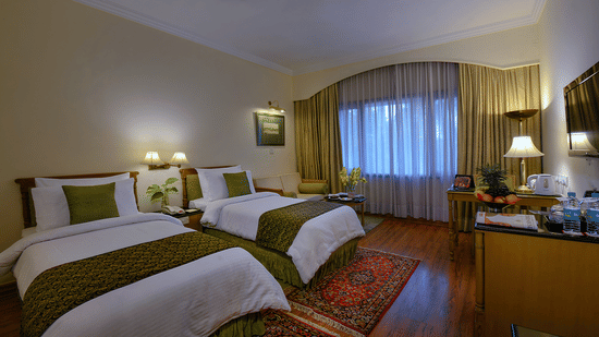A Standard Room at The Clarks Varanasi featuring twin beds with matching rugs, full-length curtains and a flat-screen television.