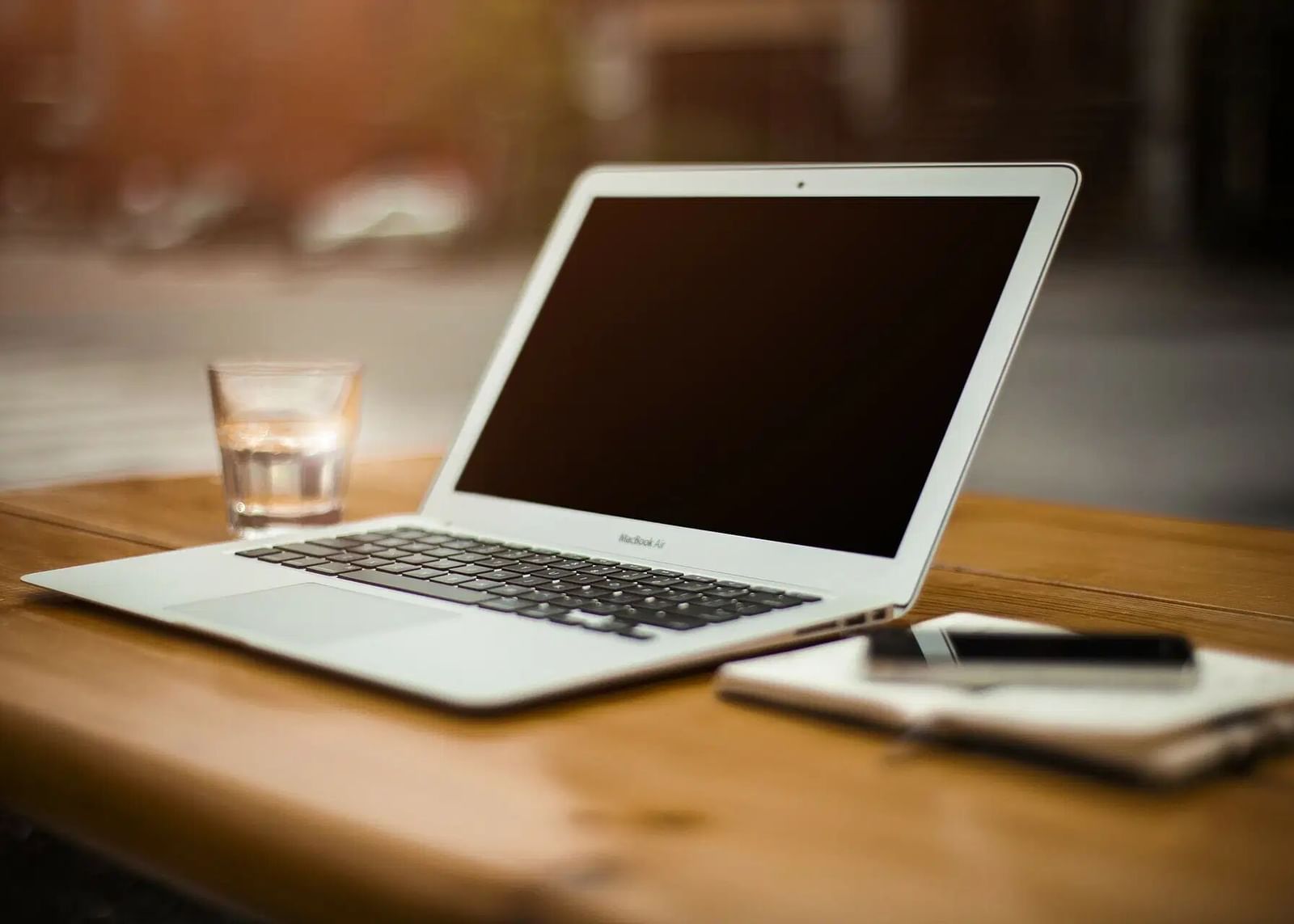 A laptop and a notebook with a pen are placed on a wooden desk.