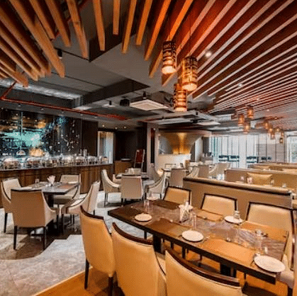 A restaurant with a fancy table setting for four and six and a buffet system towards the side, along with fancy ceiling lights at Yashshree The Imperial Inn, Siliguri.