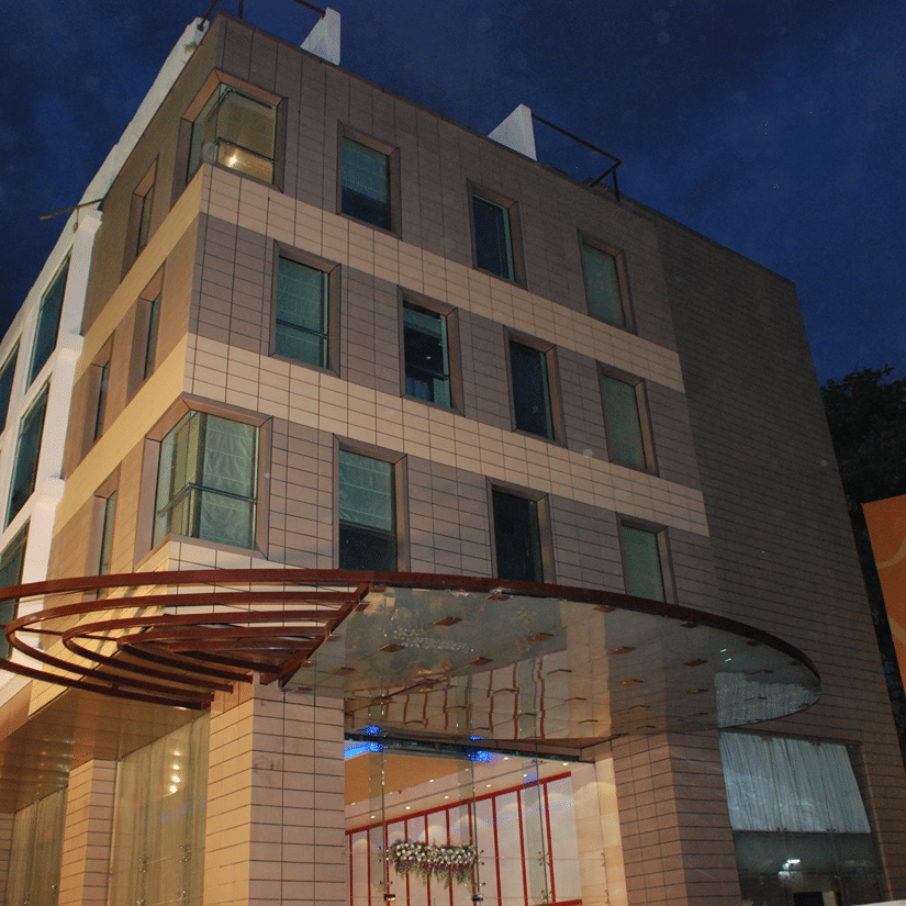 A modern multi-storey hotel stands illuminated at dusk, featuring a rounded glass canopy over its entrance - Iris Hotel Bangalore