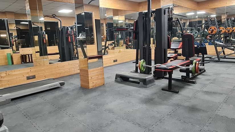 Well-equipped gym at Shaheen Bagh showcasing strength training stations and a reflective interior.