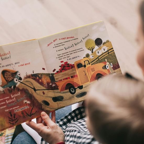 A person holds an open children's book with colourful illustrations, focusing on a picture of a truck.