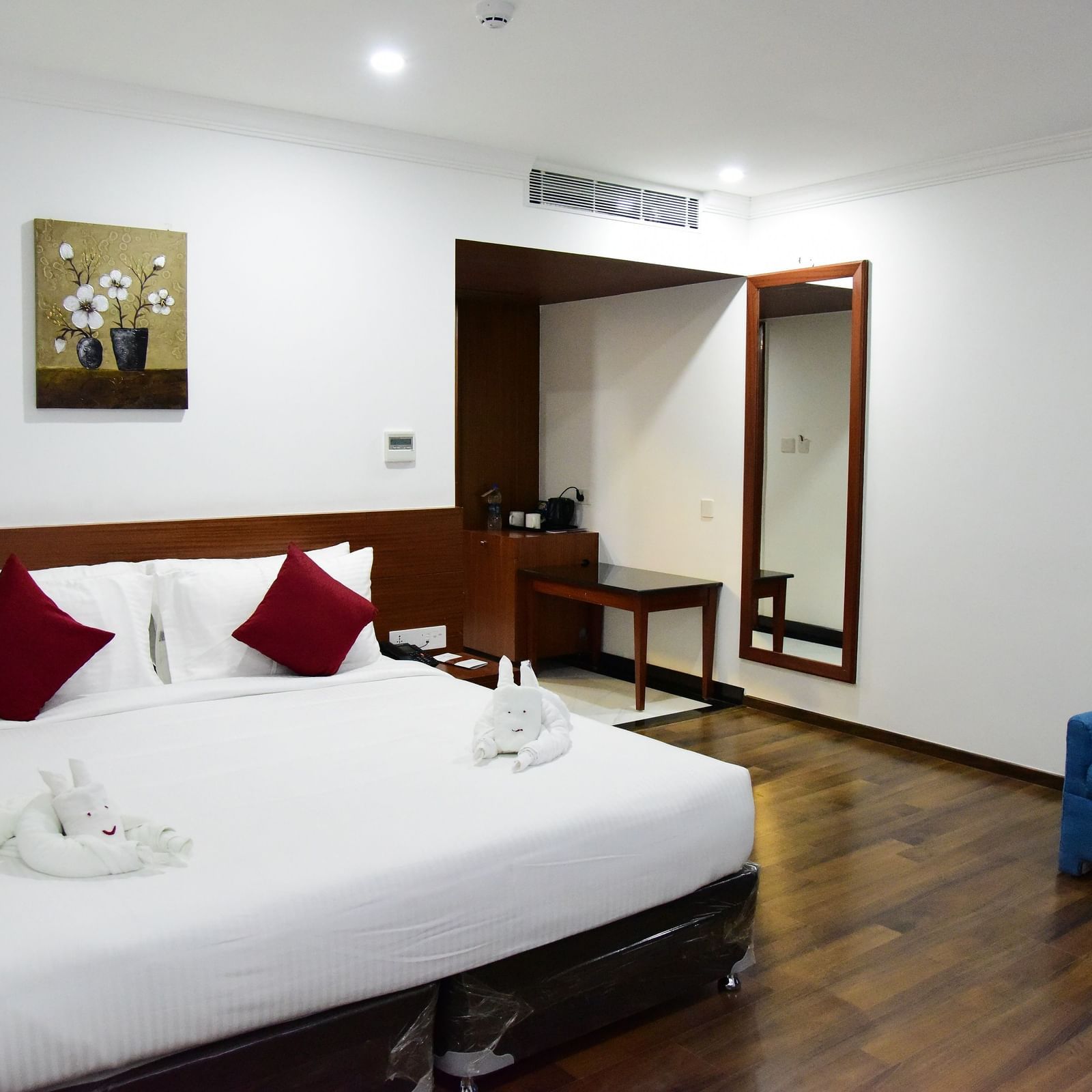 A bright and modern studio room at The Royal Comfort, featuring a comfortable bed with white linens and a stylish teal runner, along with a sleek workspace.