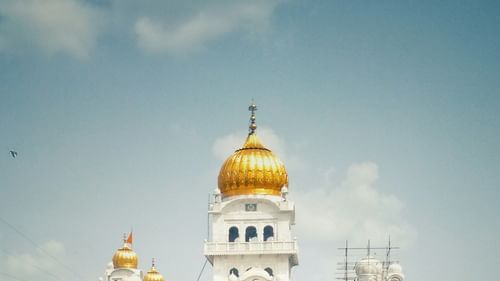 A golden and white coloured gurudwara reflected in the surrounding river under a blue sky.