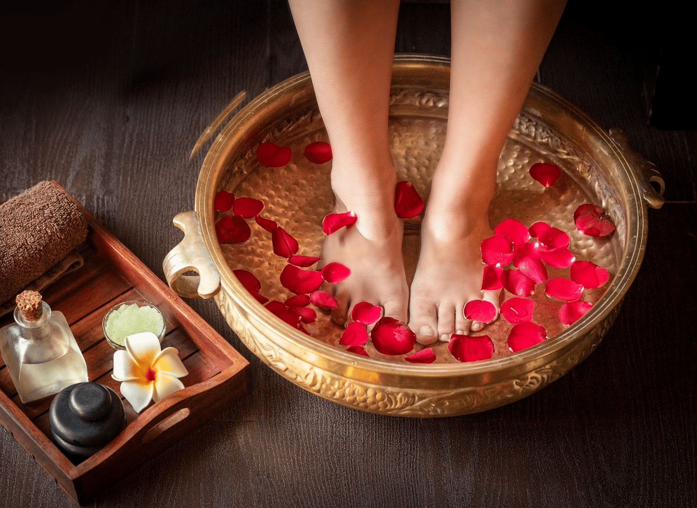 A foot soak with rose petals in a copper bowl, with aromatherapy oils and stones nearby.
