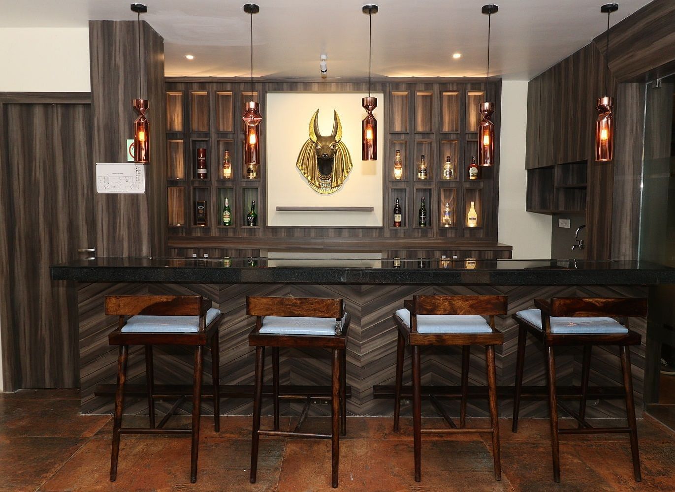 A well-stocked bar area with dark wooden counters, high bar stools, and bottles displayed on shelves, illuminated by hanging lights - Sea Hills Hotels, Sri Vijaya Puram (Port Blair)