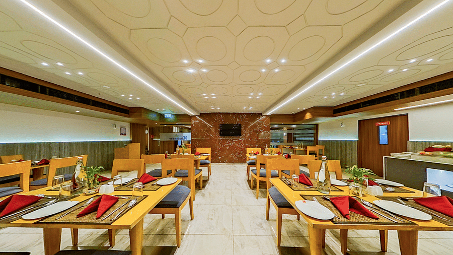 Contemporary restaurant with wooden dining tables, black chairs and red napkins at Lords Eco Inn Dahej, set for guest dining service