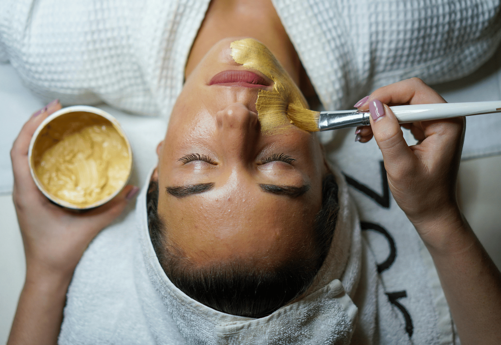 Woman receiving a facial treatment with a golden face mask applied.