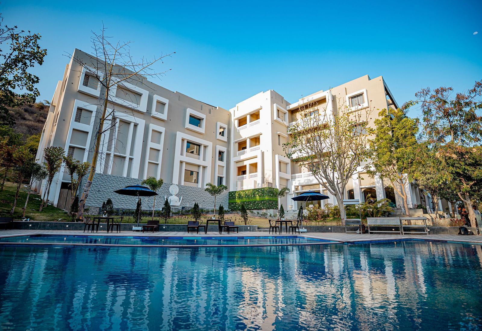 Facade of Essentia Luxury Resort and Spa, Udaipur with the pool in front of it.