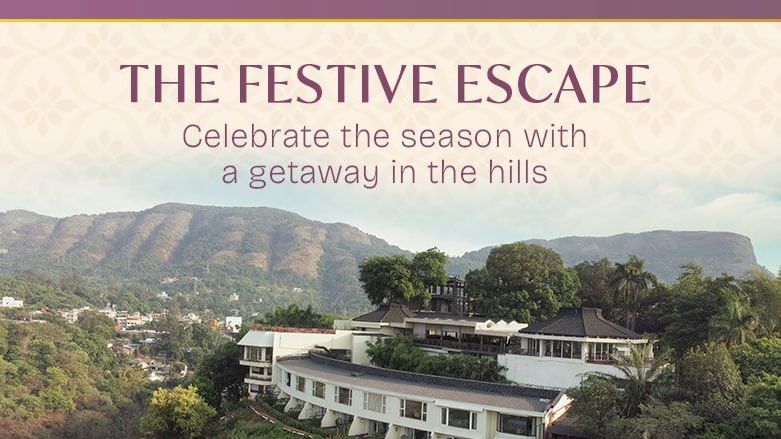 Festive campaign banner featuring a hillside hotel surrounded by greenery and mountain views. Text at the top reads - The Festive Escape – Celebrate the season with a getaway in the hills.