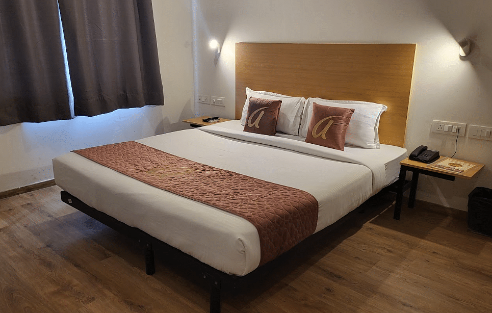 A modern hotel room featuring a double bed with white linens, brown bed runners, a wooden headboard, and warm lighting - Astra Hotels & Suites, Sarjapura