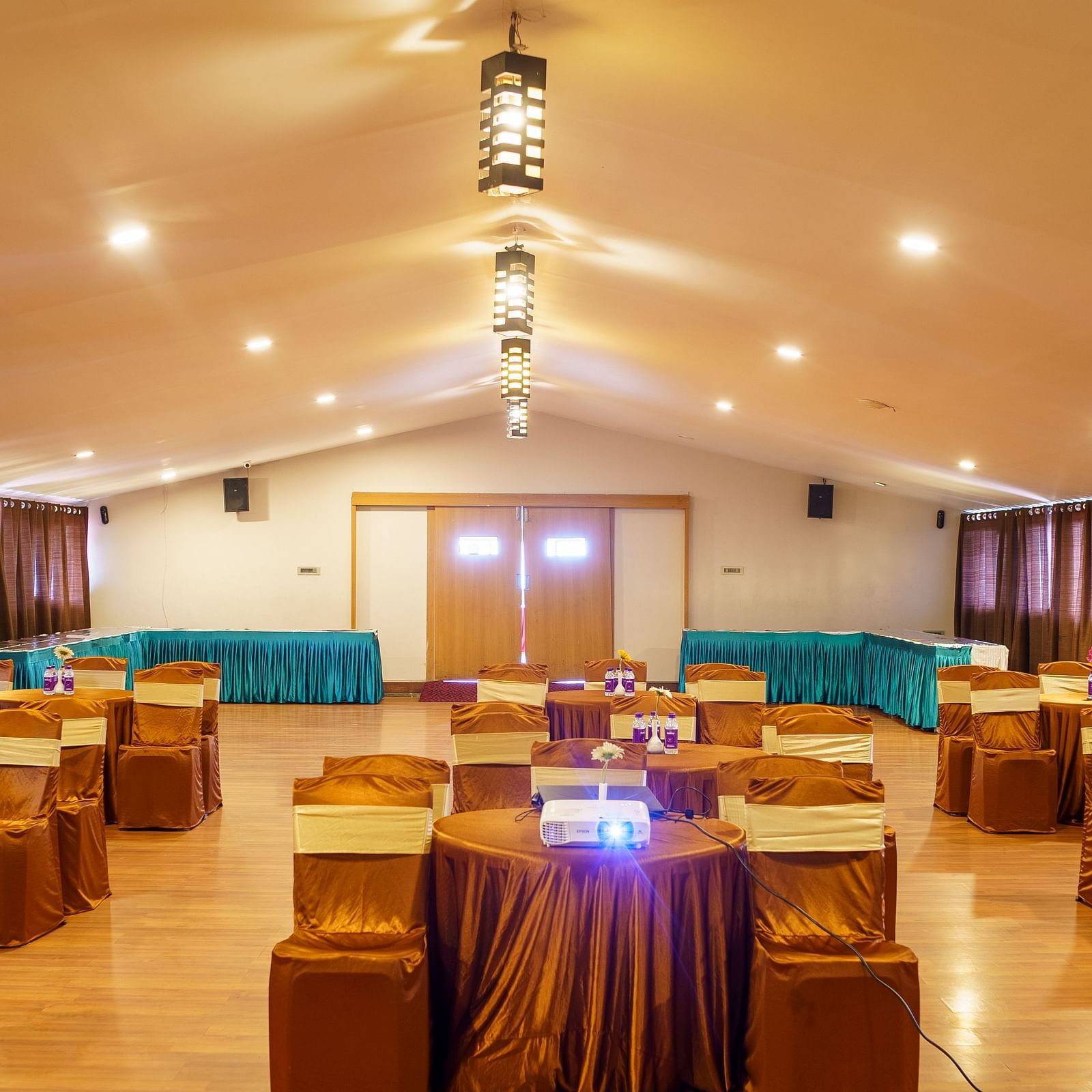 An event hall at Orsino Spa Resort with tables draped in gold fabric and chairs, under a high ceiling with multiple hanging lights.