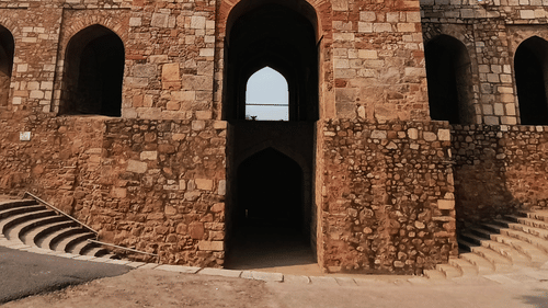 Facade view of the entrance to Chandragiri fort with arches on the side of the building and blue sky in the background.
