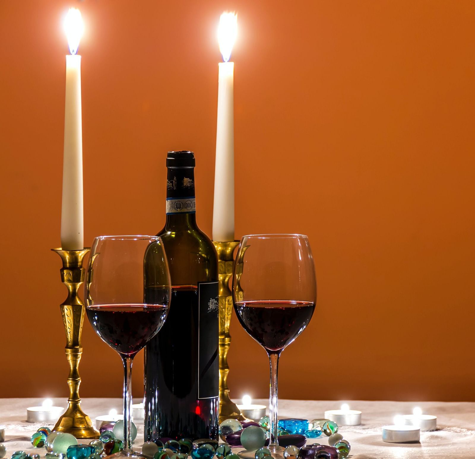 a candlelight dinner with two glasses of wine, two lit candles and a wine bottle in view