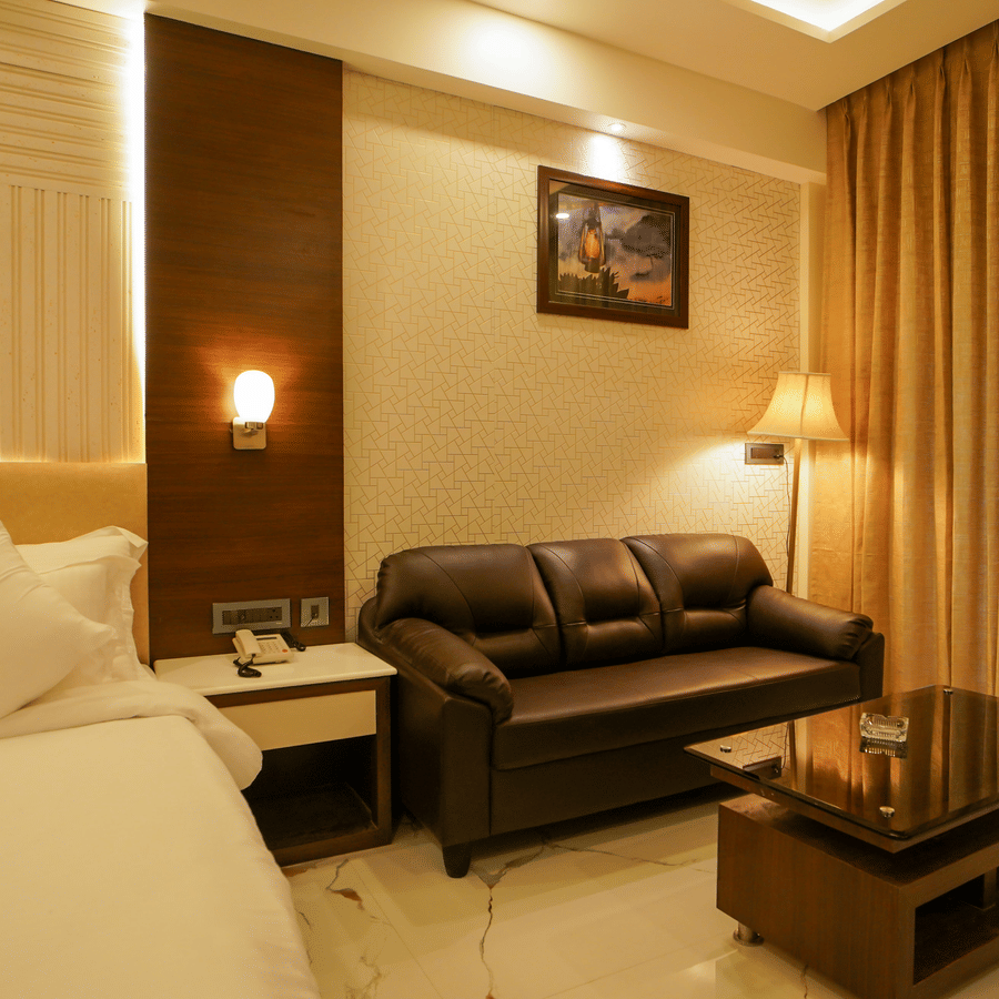 A bedroom featuring a seating area with a leather sofa and glass coffee table beside a neatly-made bed at Shanti Seaview Resort & Spa.