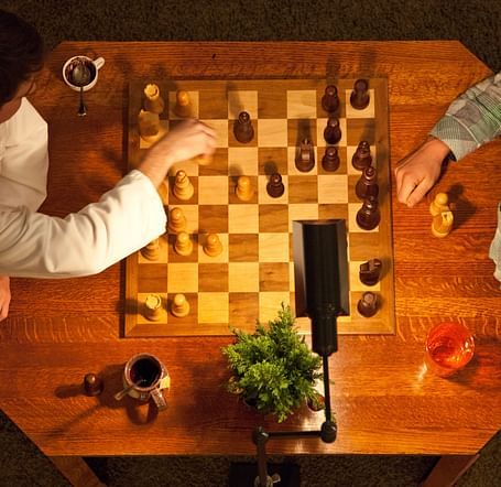 Overhead view of two people playing chess on a wooden table with warm lighting - Brewery Gulch Inn & Spa