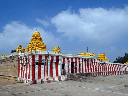 A temple structure with striped exterior walls, golden towers, and an open paved area in front.