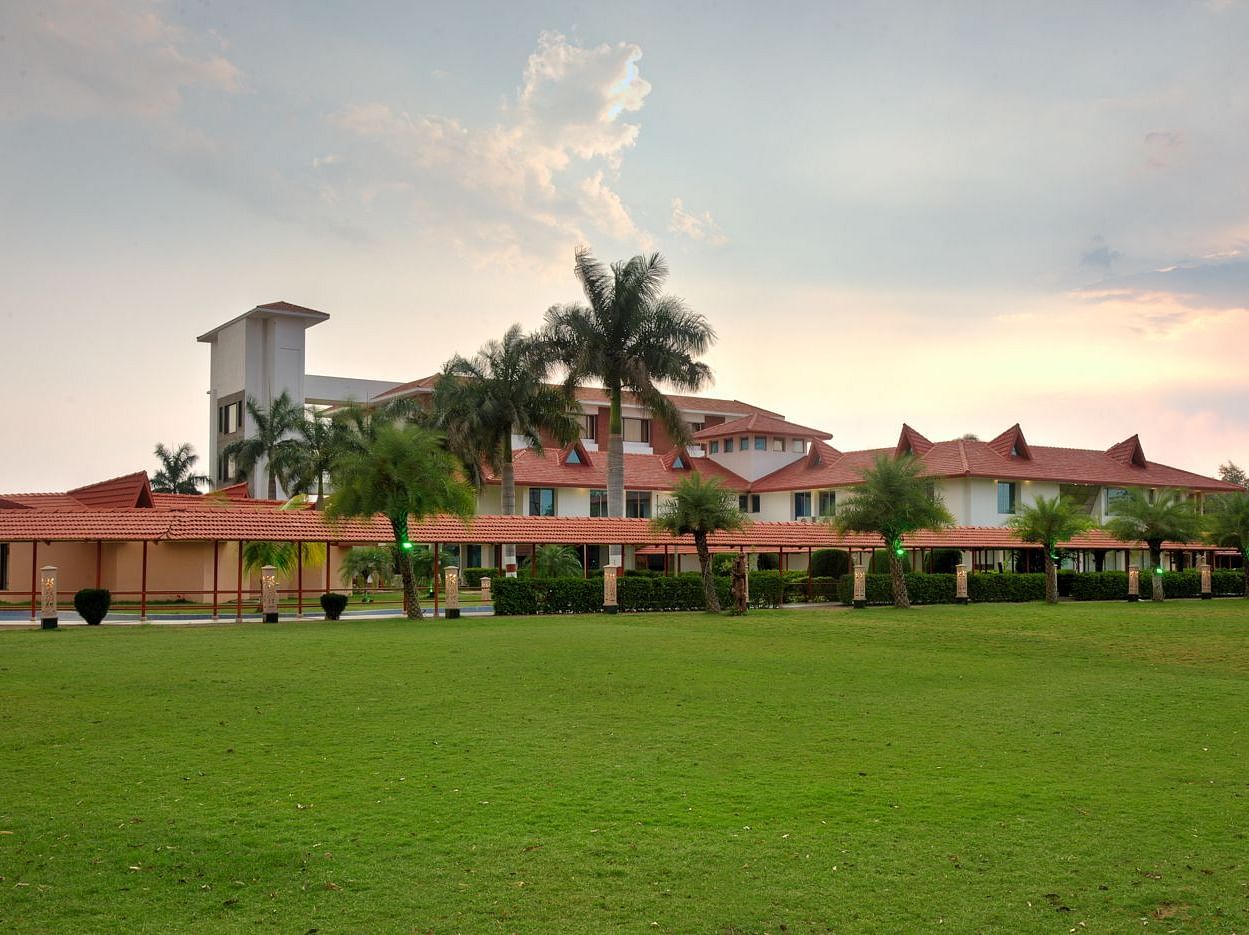 Exterior view showcasing lush grass and palm trees encircling the resort under a partly cloudy sky  | Crescent Spa & Resorts